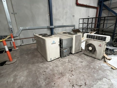 Multiple outdoor air conditioning units beside a concrete wall and metal railing in a commercial space.
