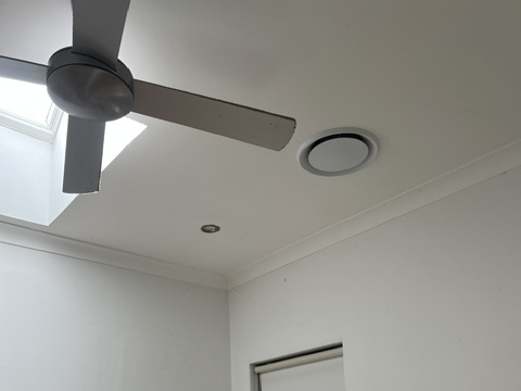 Circular ceiling air conditioning vent beside a ceiling fan in a residential room.