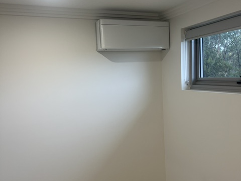 White wall-mounted split system beside a window with a blind in a residential room.